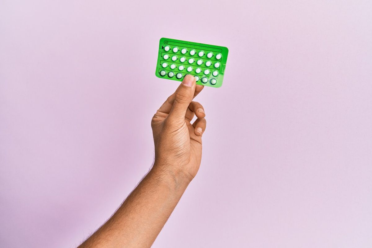 hand holding birth control pills over isolated pink background.