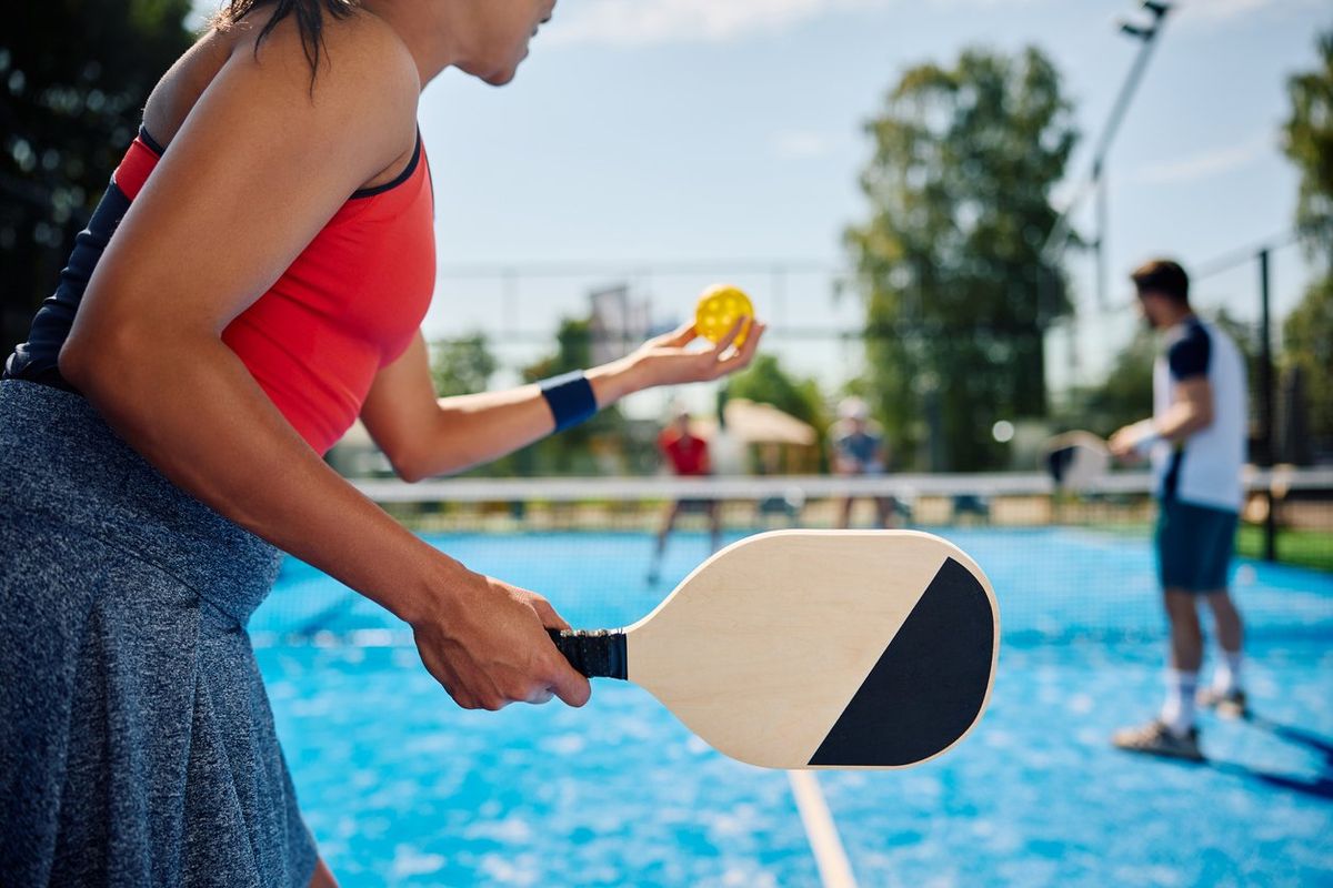 woman serving the ball while playing mixed doubles in pickleball.